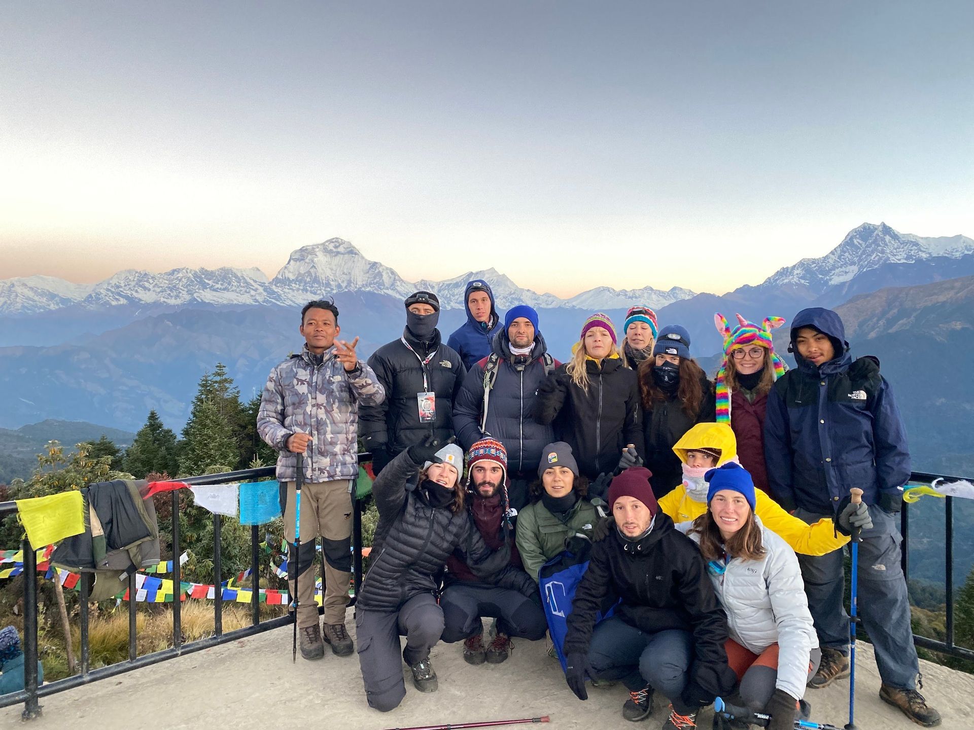 Un viaje en grupo de WeRoad posa para una foto en un mirador de montaña, con picos nevados al fondo durante el amanecer.