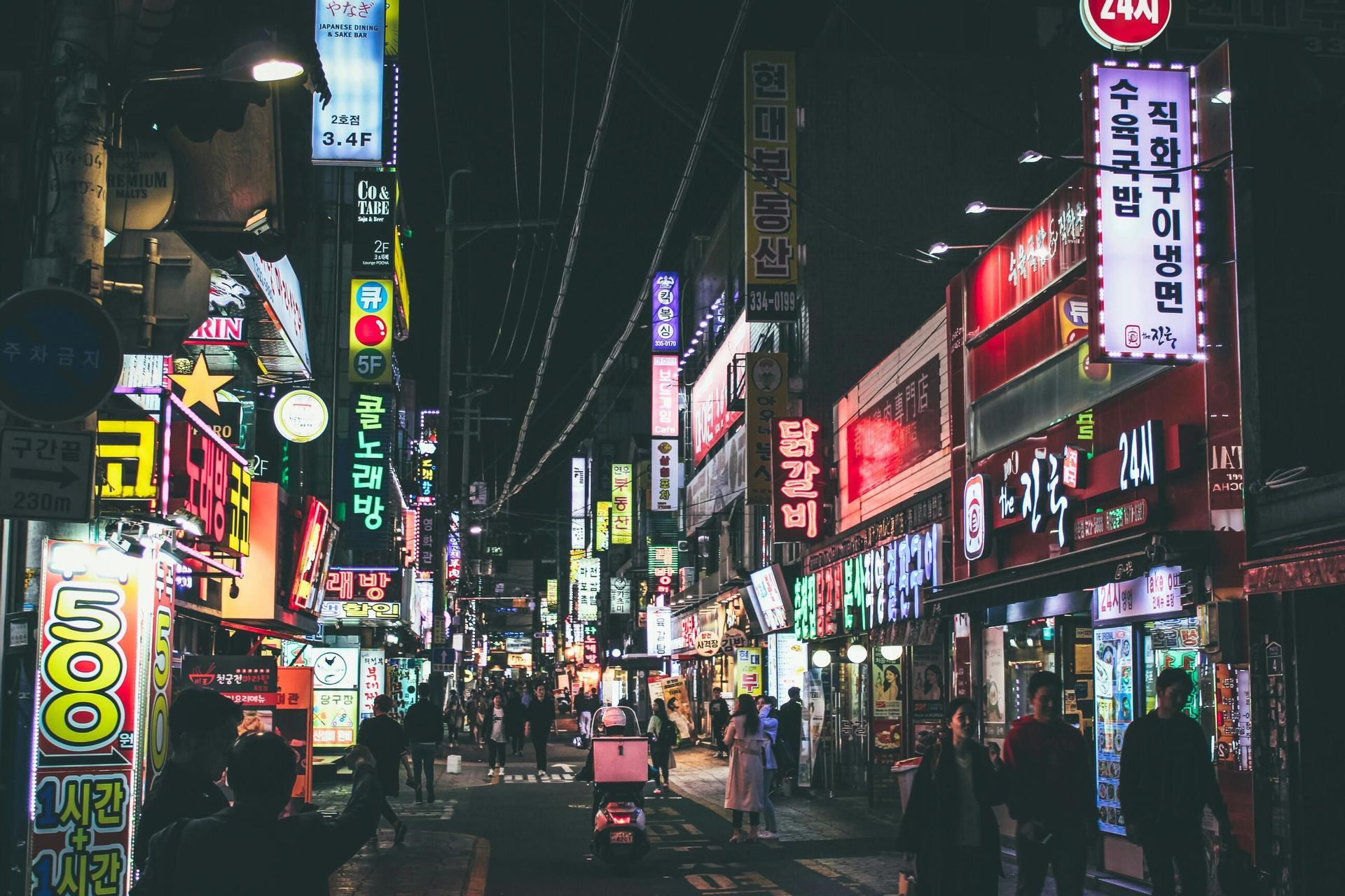 Una vivace strada cittadina di notte, con persone che passeggiano sotto edifici coperti da insegne al neon luminose e colorate con caratteri coreani