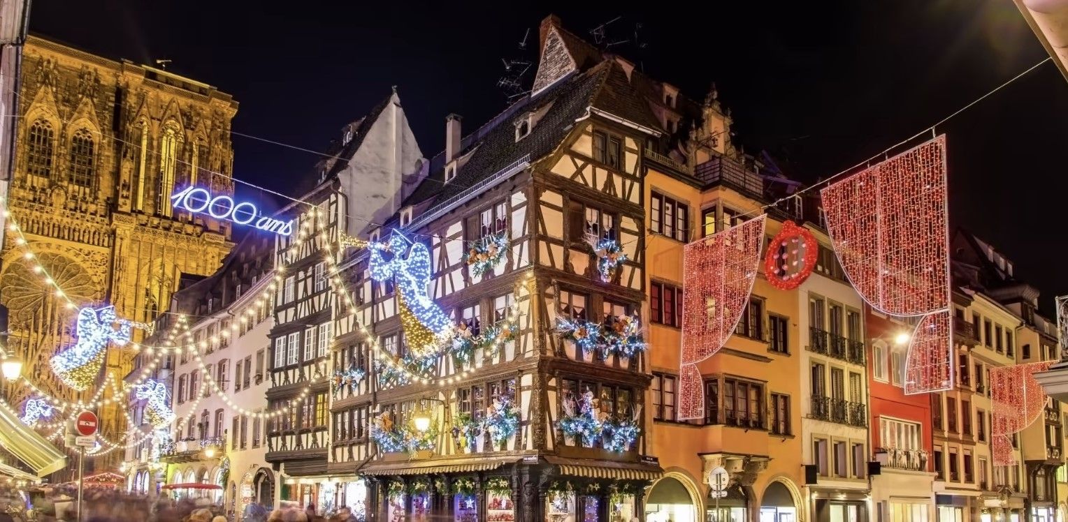 Una calle histórica con edificios de entramado de madera y una catedral decorada con luces y adornos navideños brillantes por la noche.