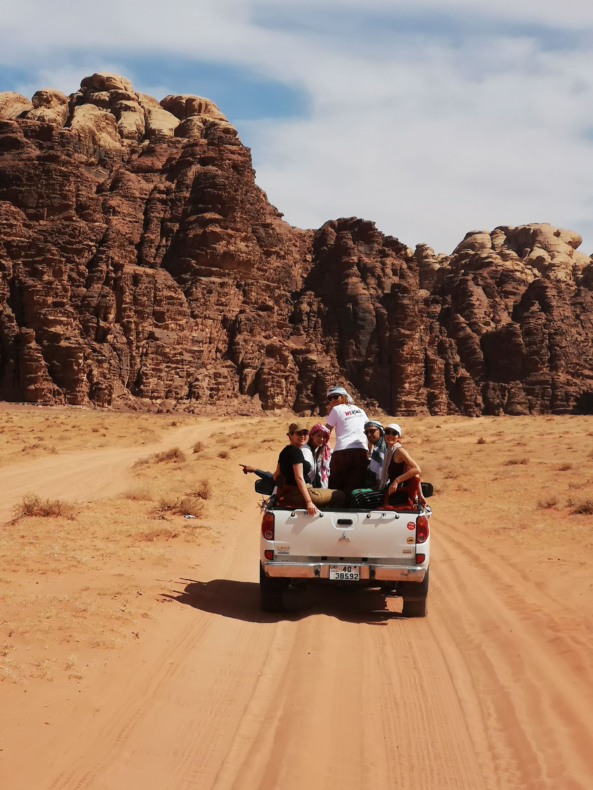 Un viaggio di gruppo WeRoad a bordo di un pickup bianco su una strada sabbiosa attraverso un deserto roccioso.