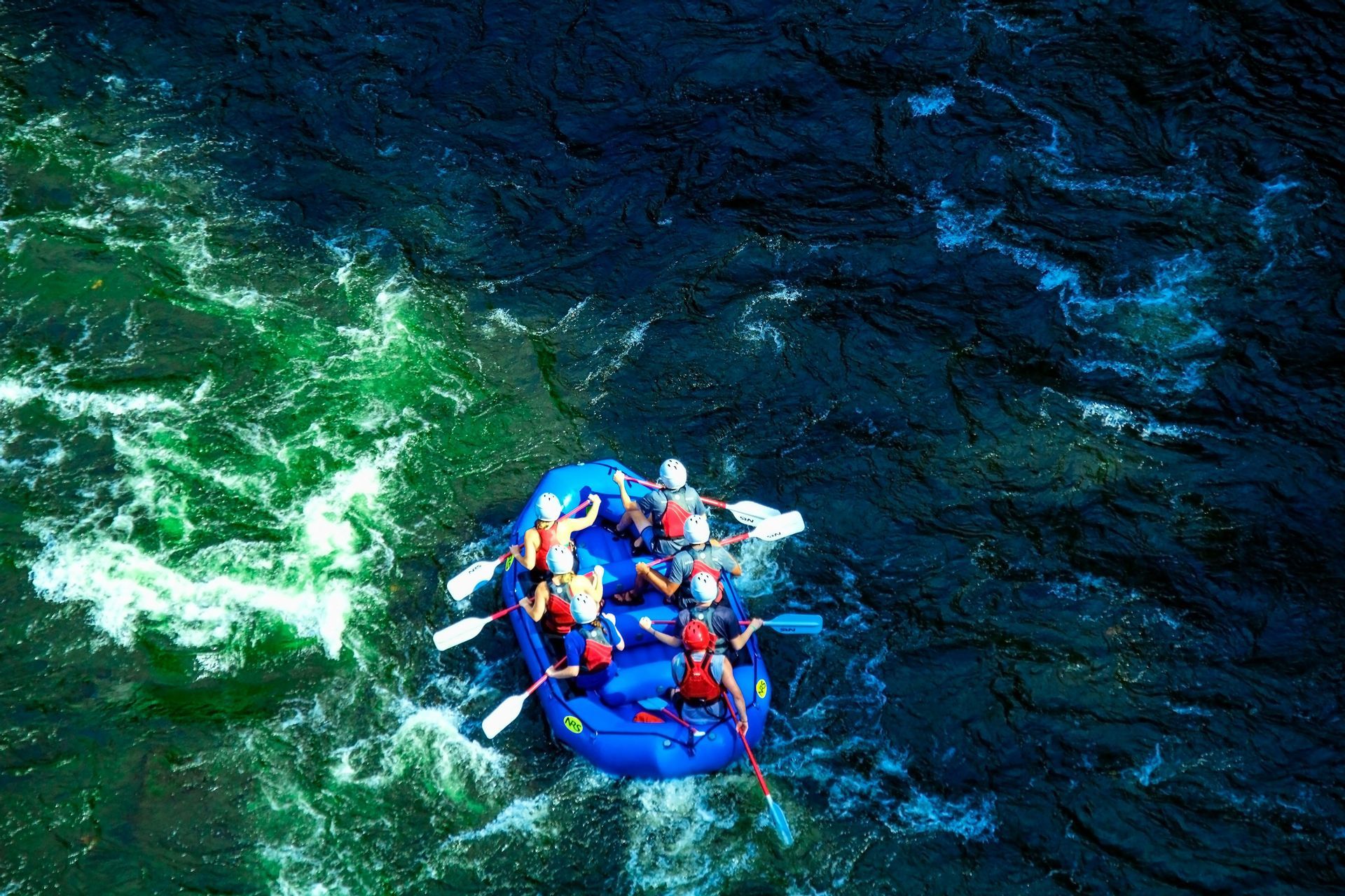 Vista aerea di un gruppo WeRoad su un gommone blu tra rapide fluviali verdi e blu.