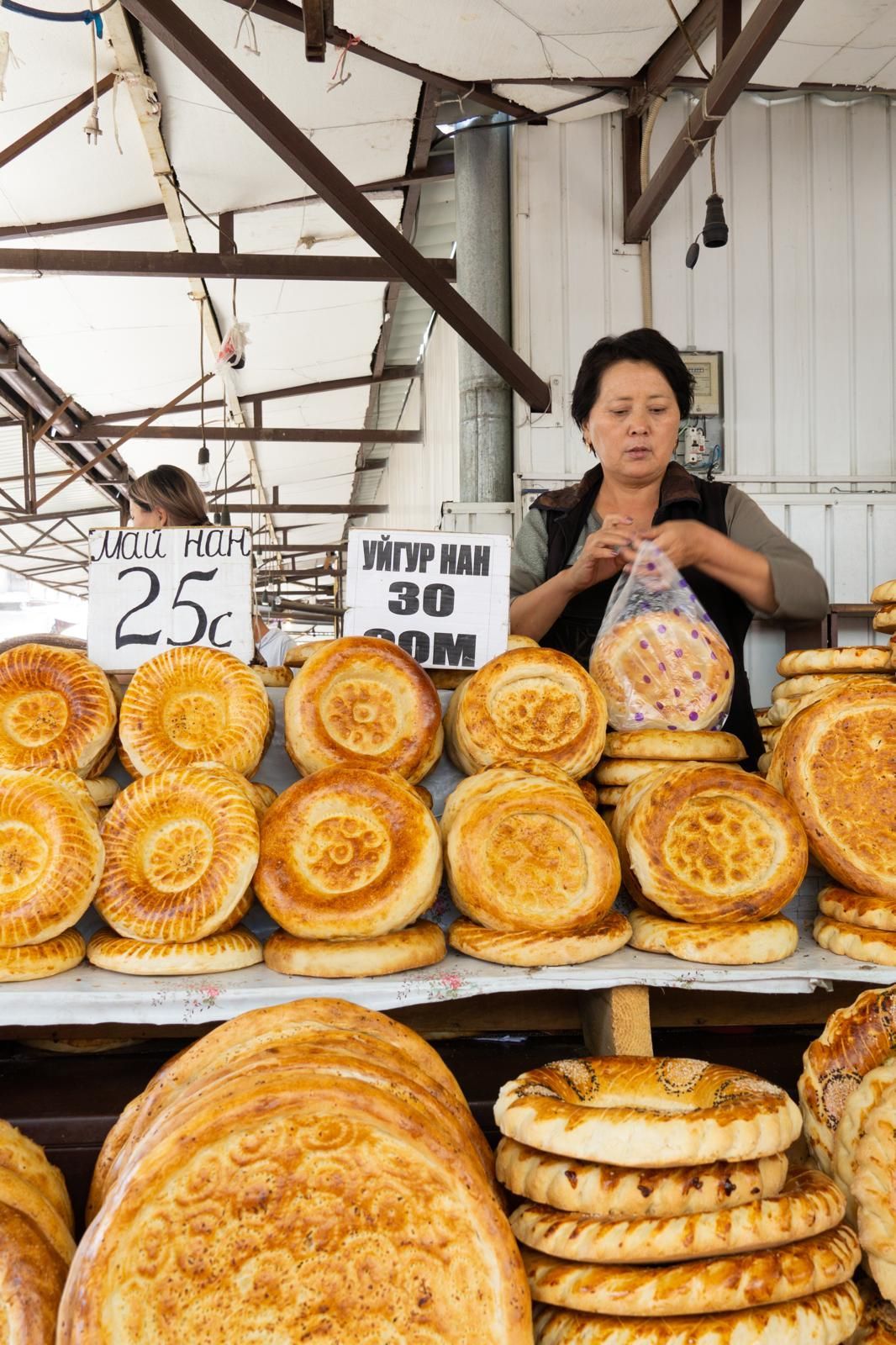 Una donna in una bancarella del mercato che vende pagnotte di pane rotonde e decorate ne mette una in un sacchetto di plastica.
