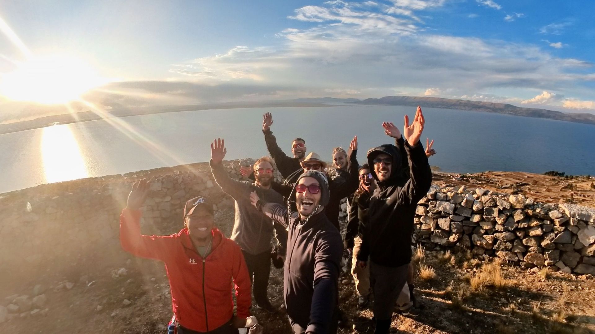 Un gruppo WeRoad in viaggio si scatta un selfie su una collina che domina un grande specchio d'acqua al tramonto.