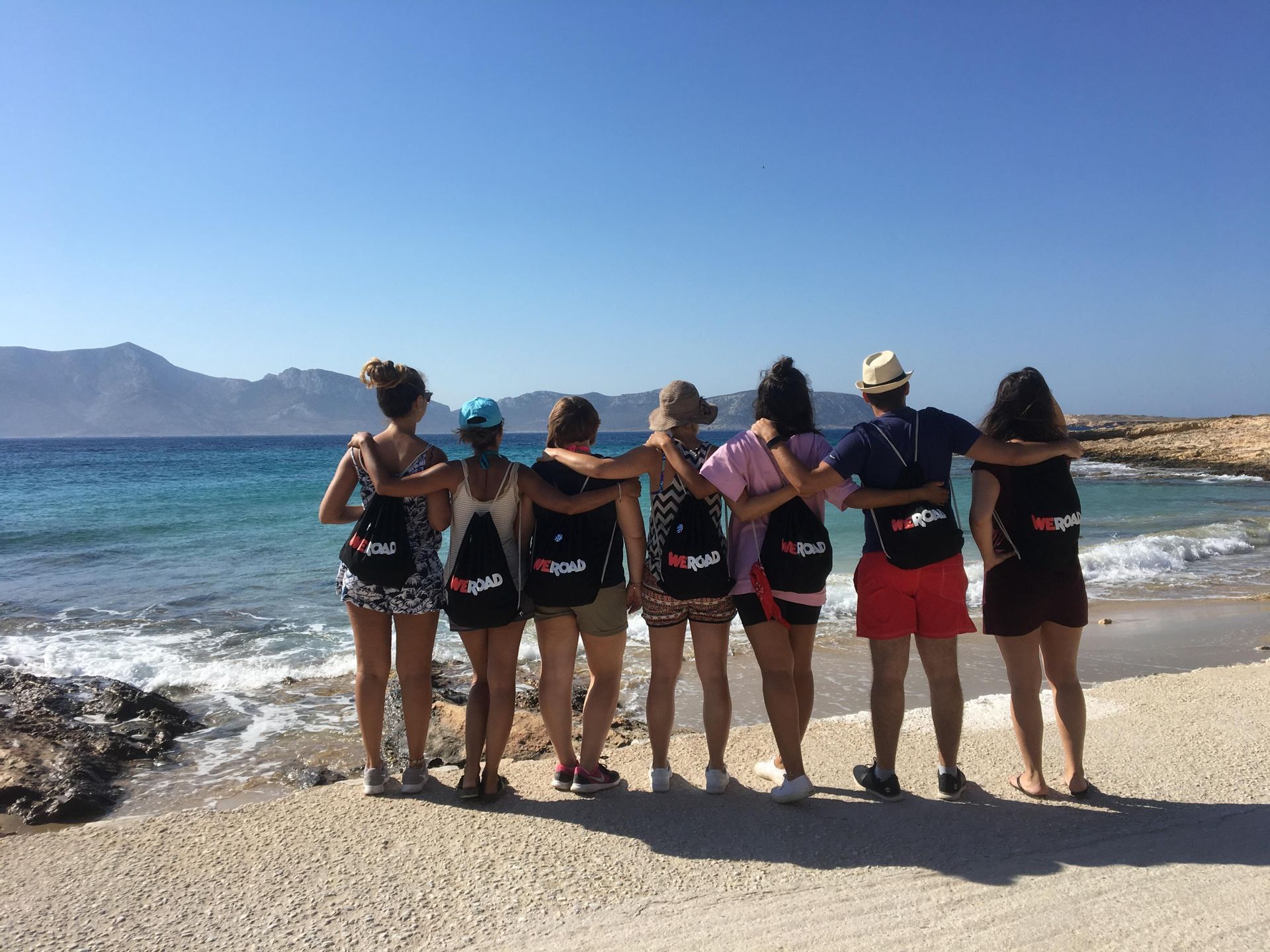Un voyage de groupe WeRoad bras dessus bras dessous sur une plage, regardant la mer