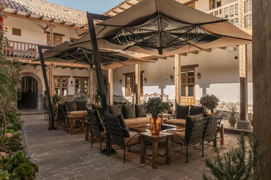 Un patio esterno con sedie a sdraio, divani e grandi ombrelloni allestito nel cortile di un edificio tradizionale.