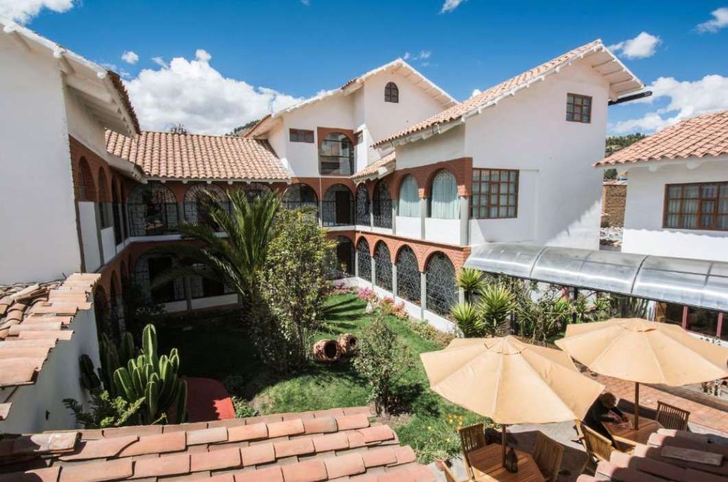 A high-angle view of a hotel courtyard with white walls, red tile roofs, brick arches, and a central garden.