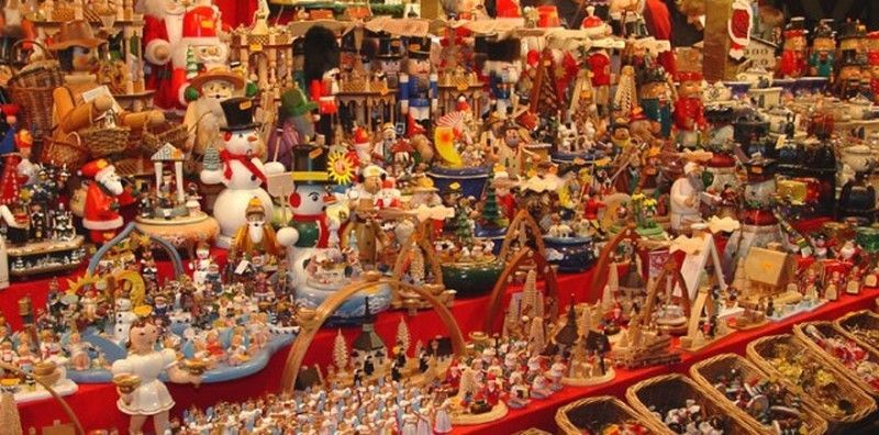 Numerosi oggetti di legno artigianali di Natale, schiaccianoci, pupazzi di neve e statuine natalizie esposti su tavoli di mercatino disposti a strati.