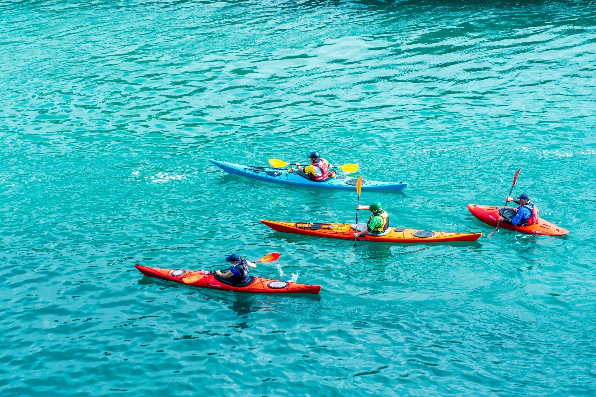 Desde arriba, cuatro personas en un viaje grupal de WeRoad reman kayaks de colores en aguas turquesas.