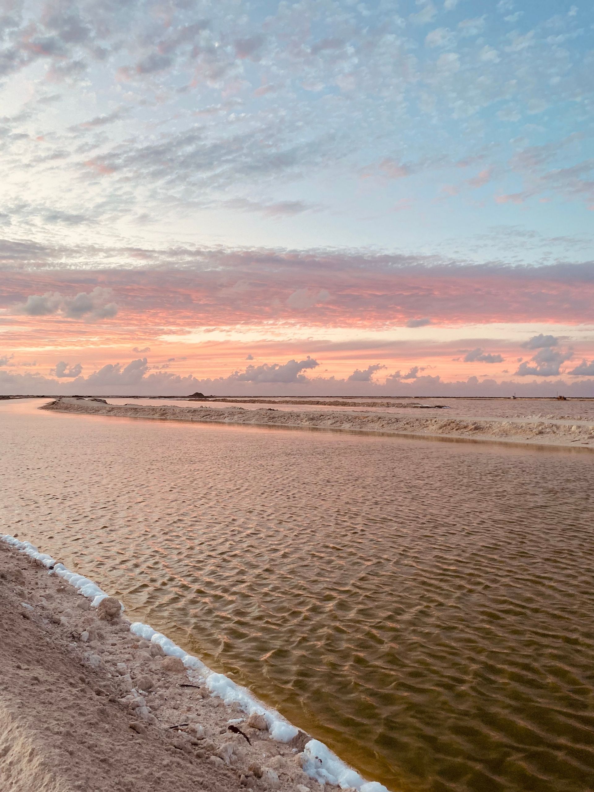 Saline con canali d'acqua che riflettono un cielo al tramonto colorato di rosa e blu.
