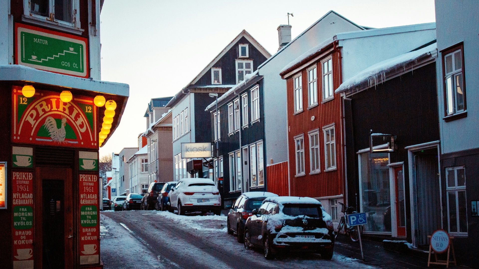 Una strada innevata fiancheggiata da edifici colorati e auto parcheggiate in una città d'inverno.