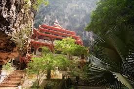 Un templo rojo tradicional de varios niveles, construido en un acantilado rocoso y rodeado de exuberante vegetación selvática.