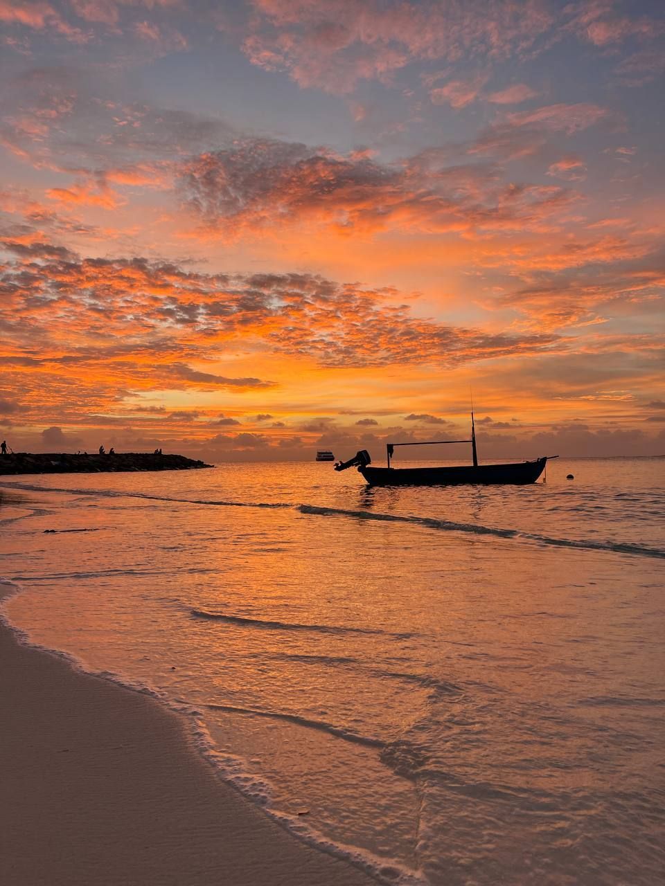 Una barca in controluce galleggia sul mare vicino a una spiaggia sabbiosa sotto un cielo arancione intenso al tramonto.