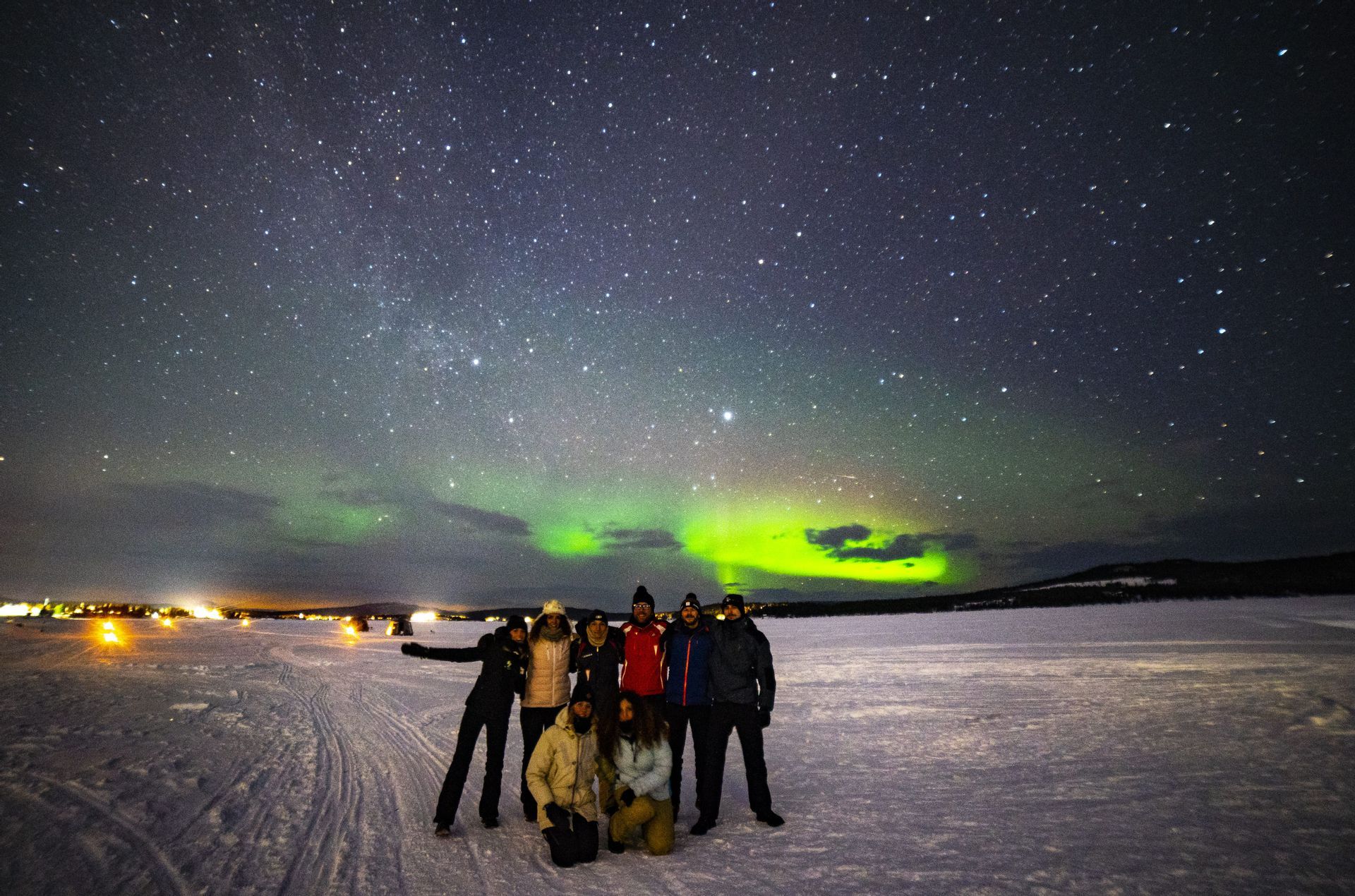 Un gruppo WeRoad in viaggio posa su una piana innevata di notte, con l'aurora boreale e le stelle visibili nel cielo.