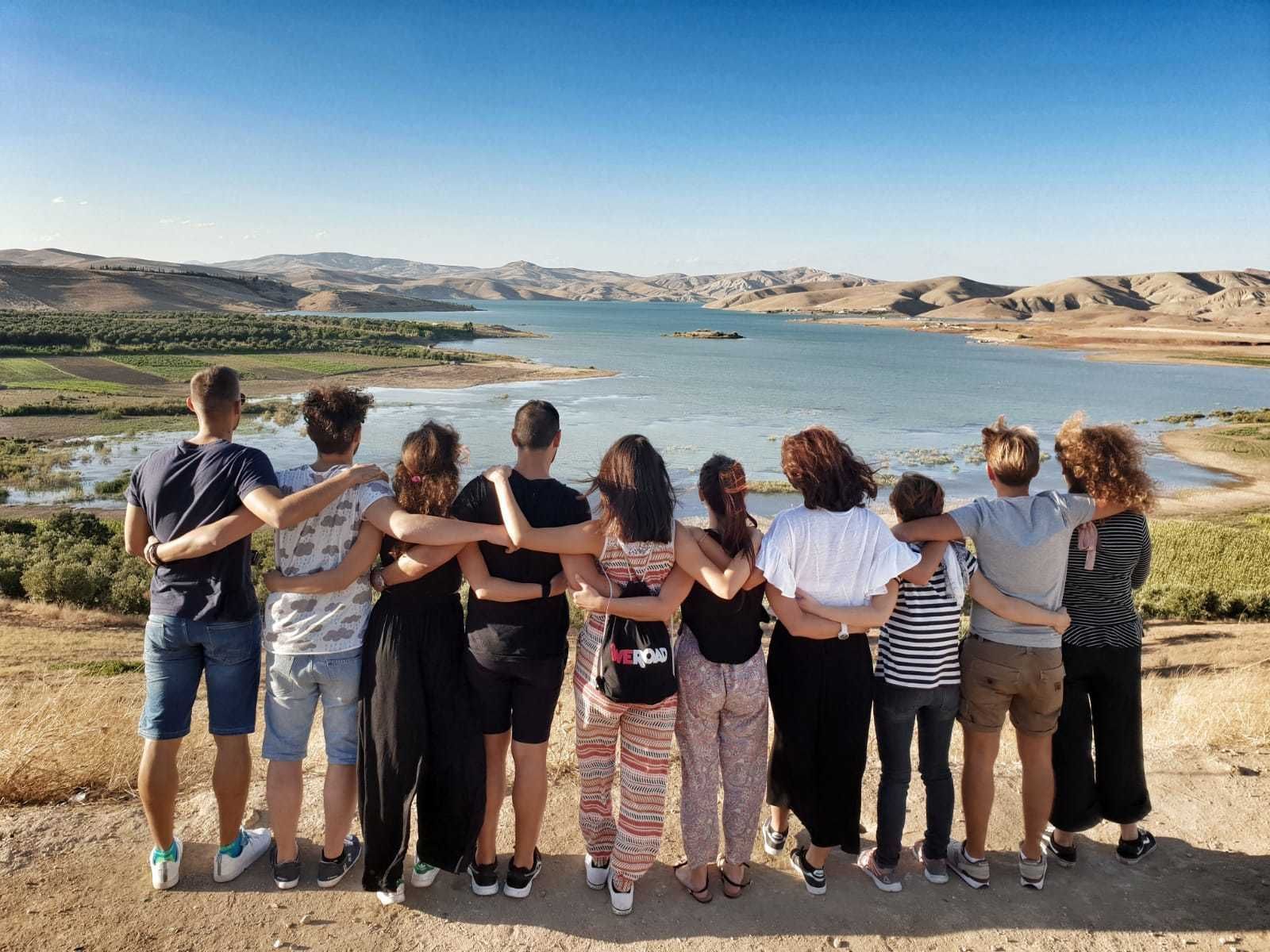 Eine WeRoad-Gruppe steht Arm in Arm und blickt über einen See, der von sanften Hügeln umgeben ist.