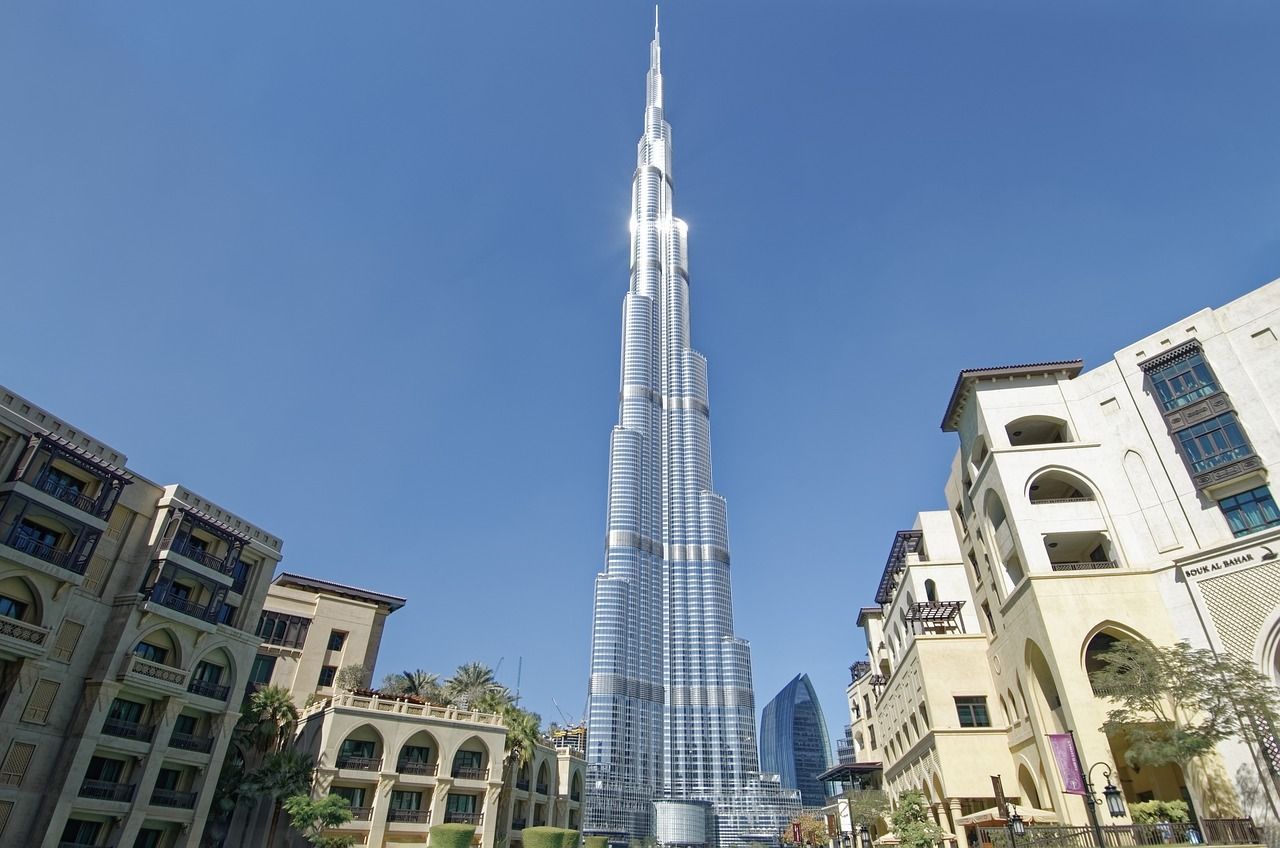 Un moderno grattacielo di vetro si erge su edifici in stile tradizionale sotto un cielo azzurro brillante.