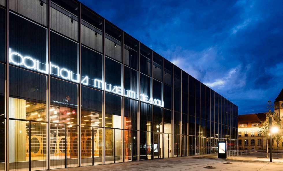 La moderna facciata in vetro del Bauhaus Museum Dessau illuminata di notte, con la sua insegna al neon che brilla contro un cielo blu scuro.