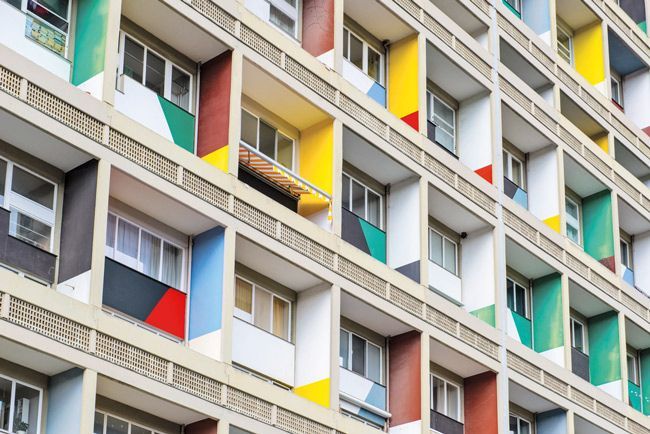 La facciata di un moderno edificio residenziale con una griglia di balconi in cemento dipinti con colori primari vivaci.