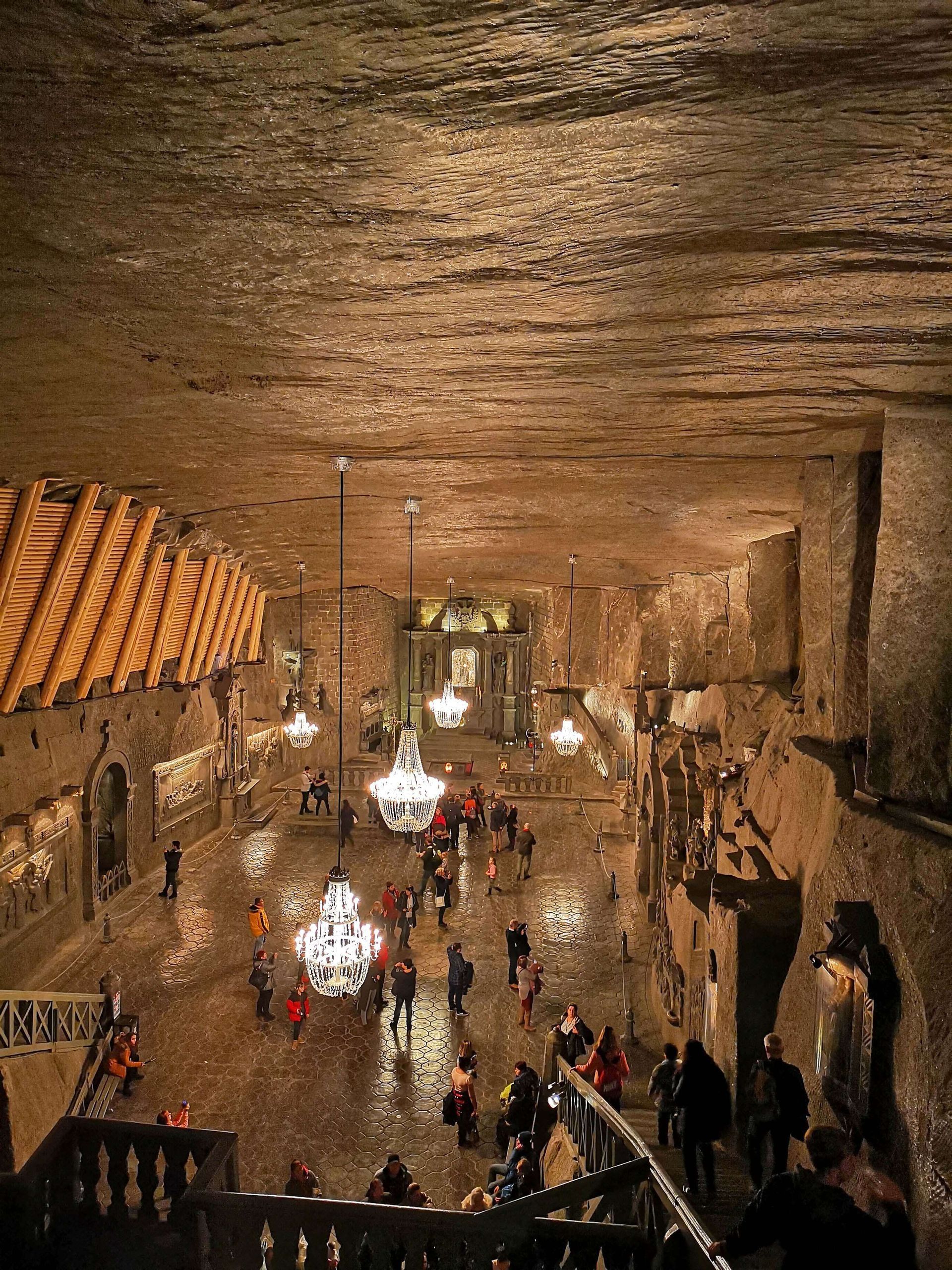 Un viaje en grupo de WeRoad visita una vasta catedral subterránea tallada en la roca, iluminada por grandes candelabros de cristal, vista desde arriba.