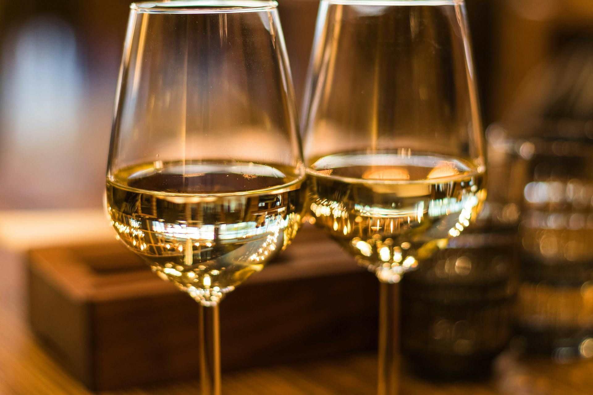 Un primo piano di due bicchieri di vino bianco, che riflettono le luci calde e soffuse della stanza.