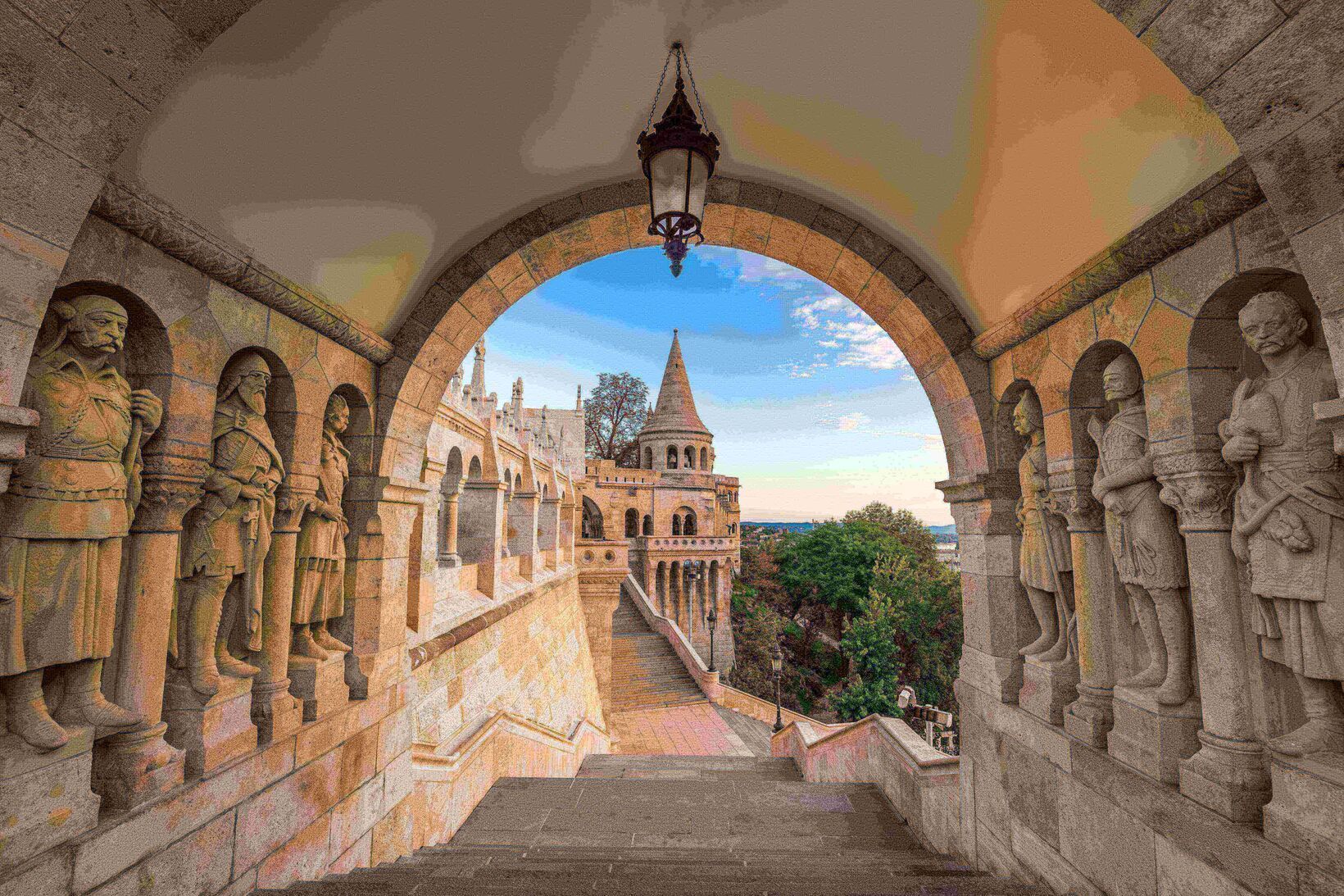 Blick auf eine steinerne Bastei mit spitzem Turm, gesehen unter einem großen, mit Ritterstatuen gesäumten Torbogen.