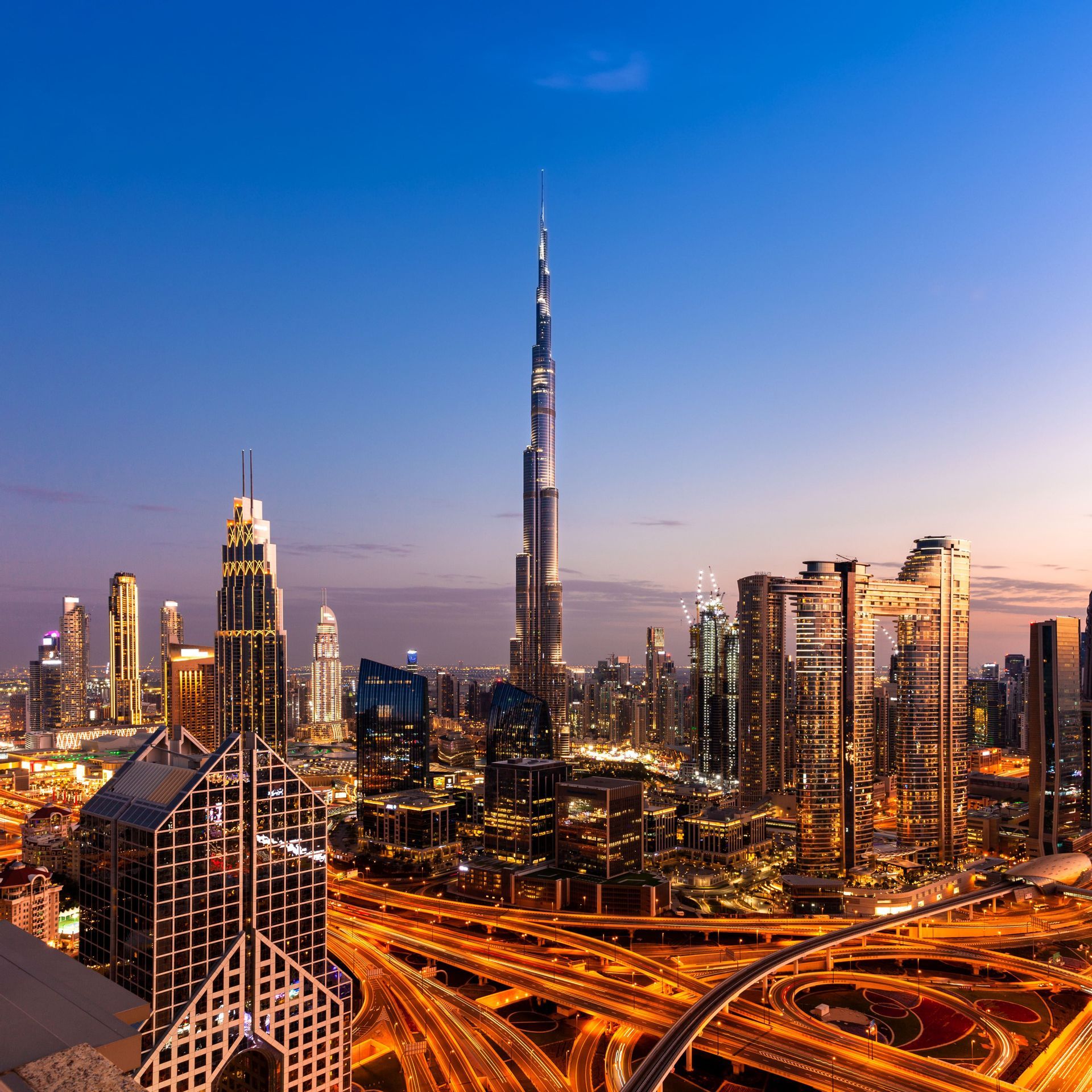 Lo skyline di Dubai, con il Burj Khalifa e altri grattacieli, illuminato al tramonto con scie luminose sulle autostrade sottostanti.