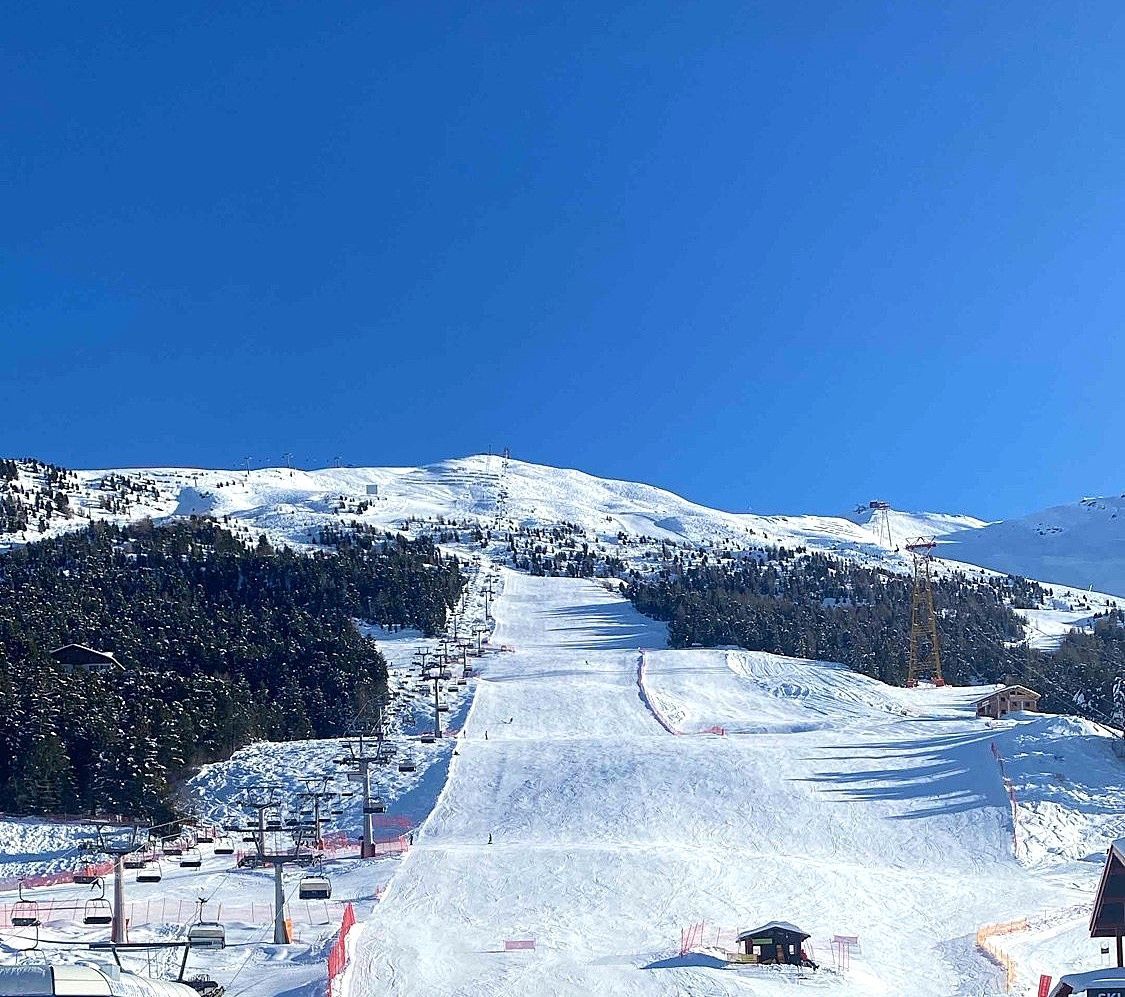 Un'ampia veduta di una montagna innevata con piste da sci e seggiovie sotto un cielo azzurro e limpido.