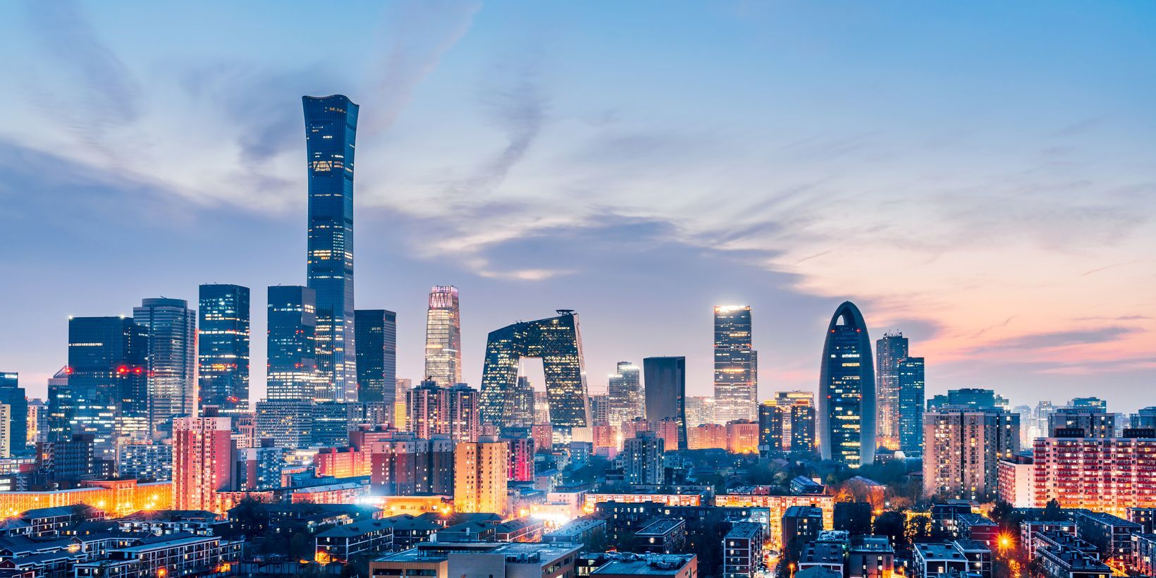 Vue panoramique sur une skyline urbaine moderne, avec de nombreux gratte-ciel illuminés sous un ciel de crépuscule coloré.