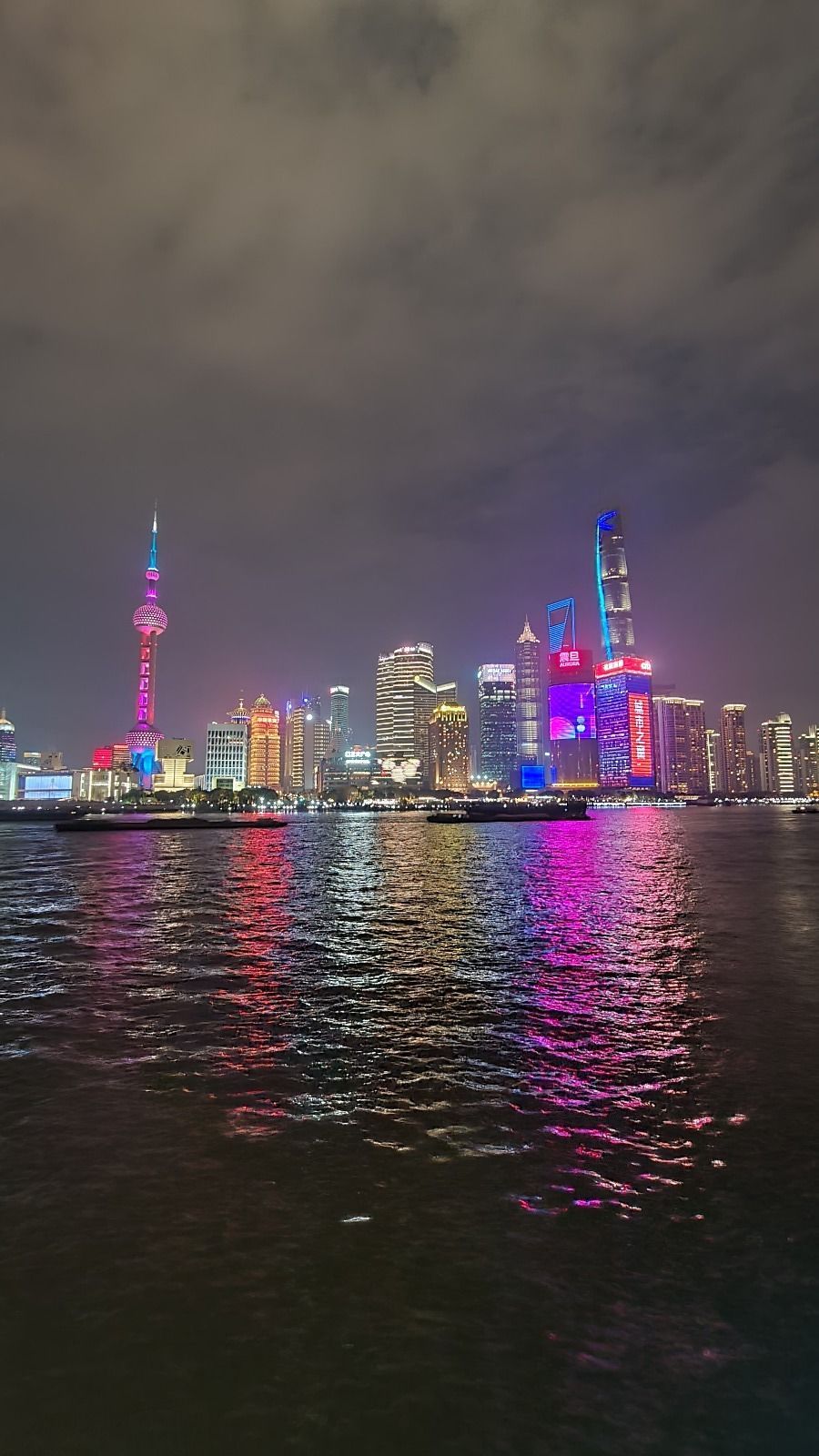 Uno skyline moderno di città di notte, con grattacieli illuminati da luci rosa e blu che si riflettono sull'acqua sottostante.