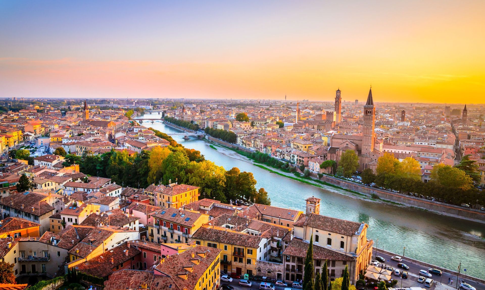 Vista aerea di una città storica con tetti rossi e un fiume sinuoso sotto un cielo dorato al tramonto.