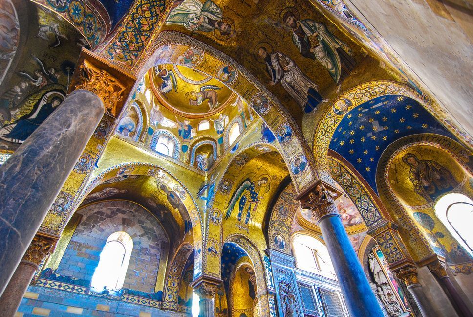 L'interno sontuoso di una chiesa con mosaici dorati e blu su volte e archi sostenuti da colonne di marmo.