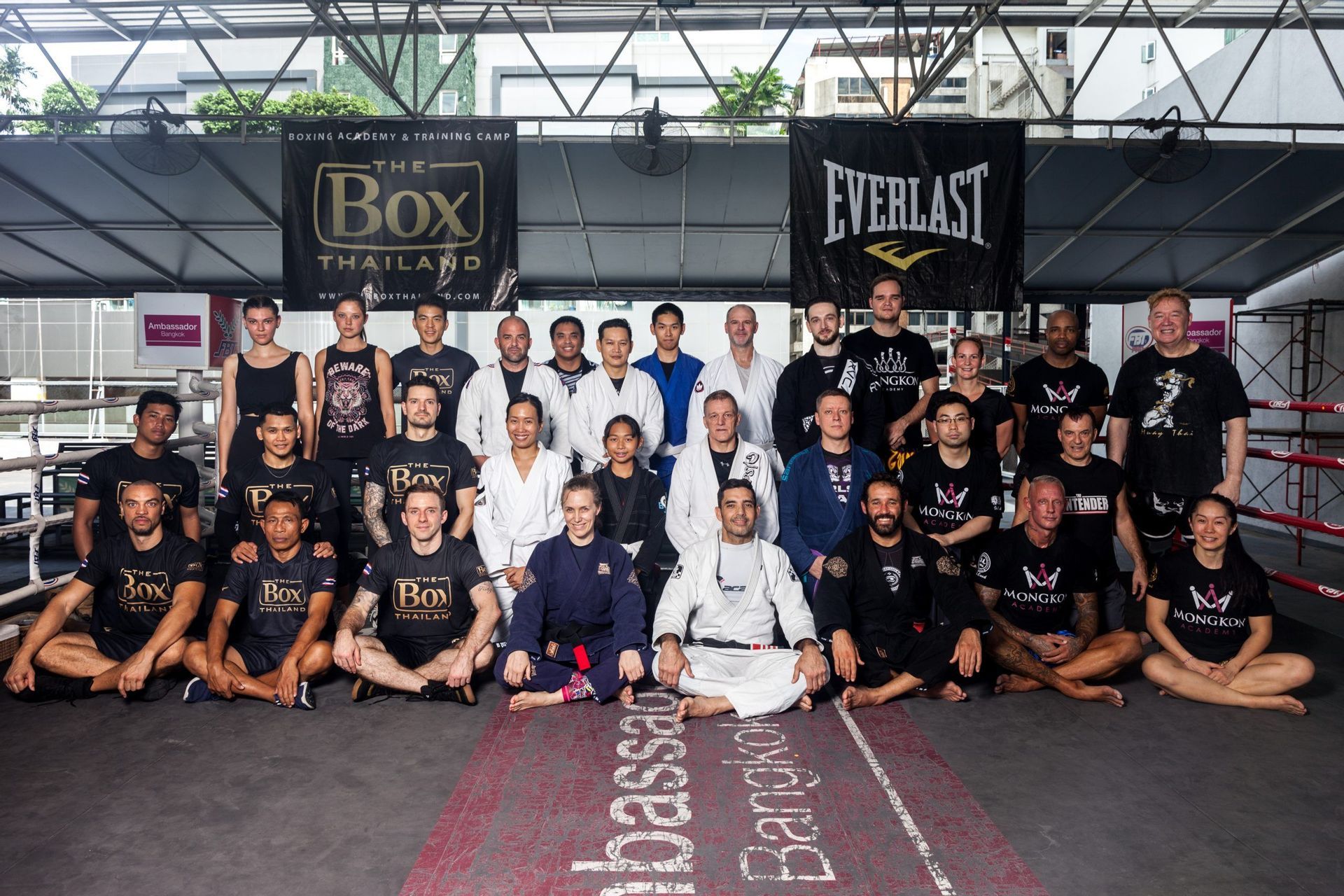 Un grand groupe de personnes en tenue de sport et kimonos d'arts martiaux posant pour une photo de groupe dans une salle de boxe.