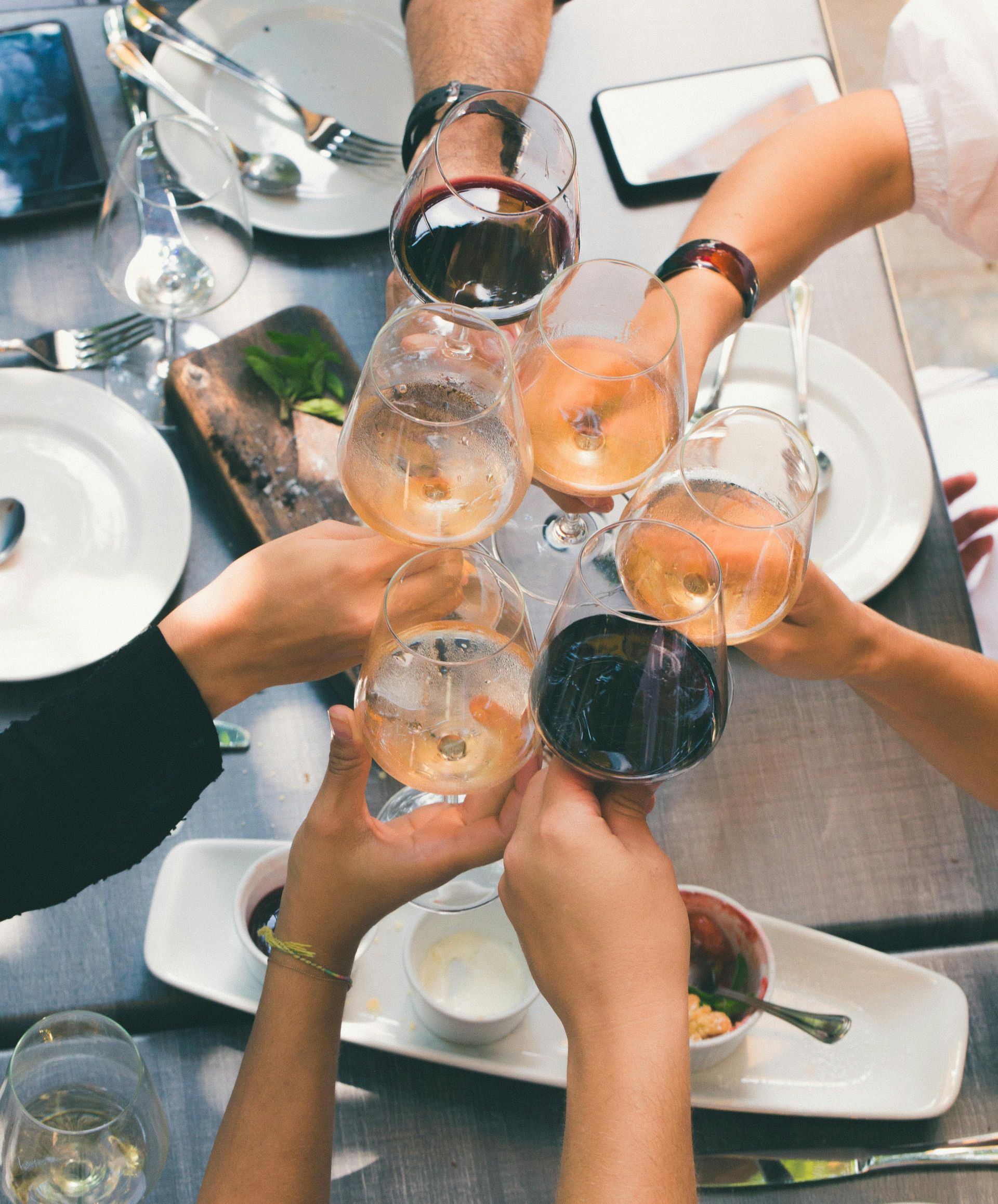 Ripresa dall'alto di un viaggio di gruppo WeRoad che brinda con calici di vino rosso, bianco e rosé attorno a un tavolo da cena.