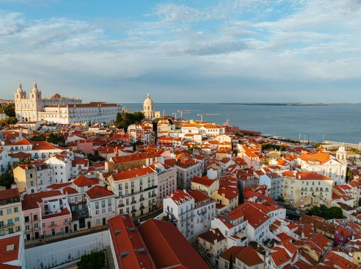 Una vista aerea di una storica città costiera, che mostra tetti rossi e edifici bianchi che scendono verso l'acqua.