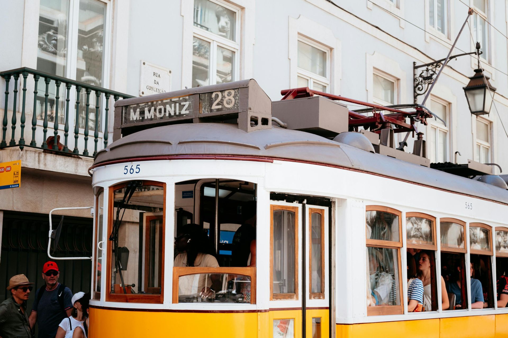 Un classico tram giallo e bianco, numero 28, che trasporta passeggeri su una strada cittadina di fronte a un edificio bianco.