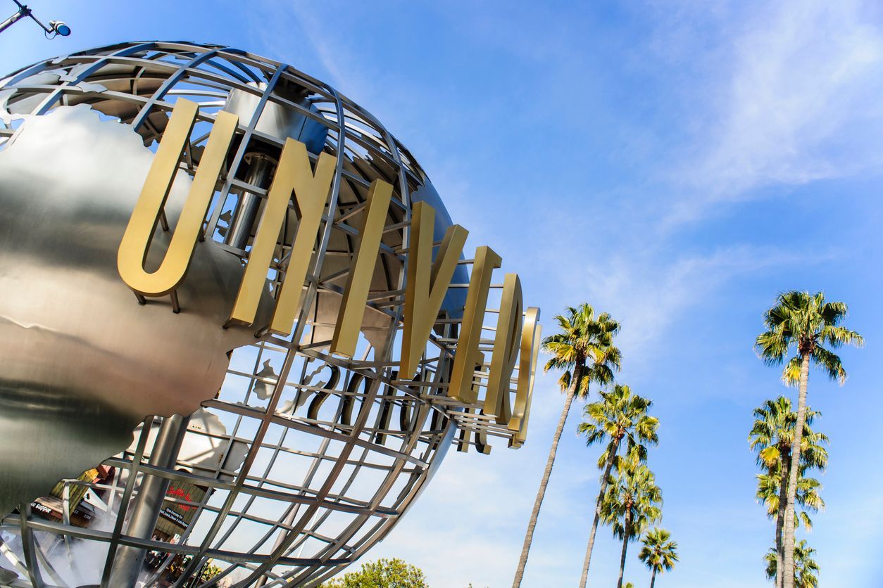 Una ripresa dal basso del logo a globo degli Universal Studios con le sue grandi lettere dorate e palme sullo sfondo di un cielo azzurro.