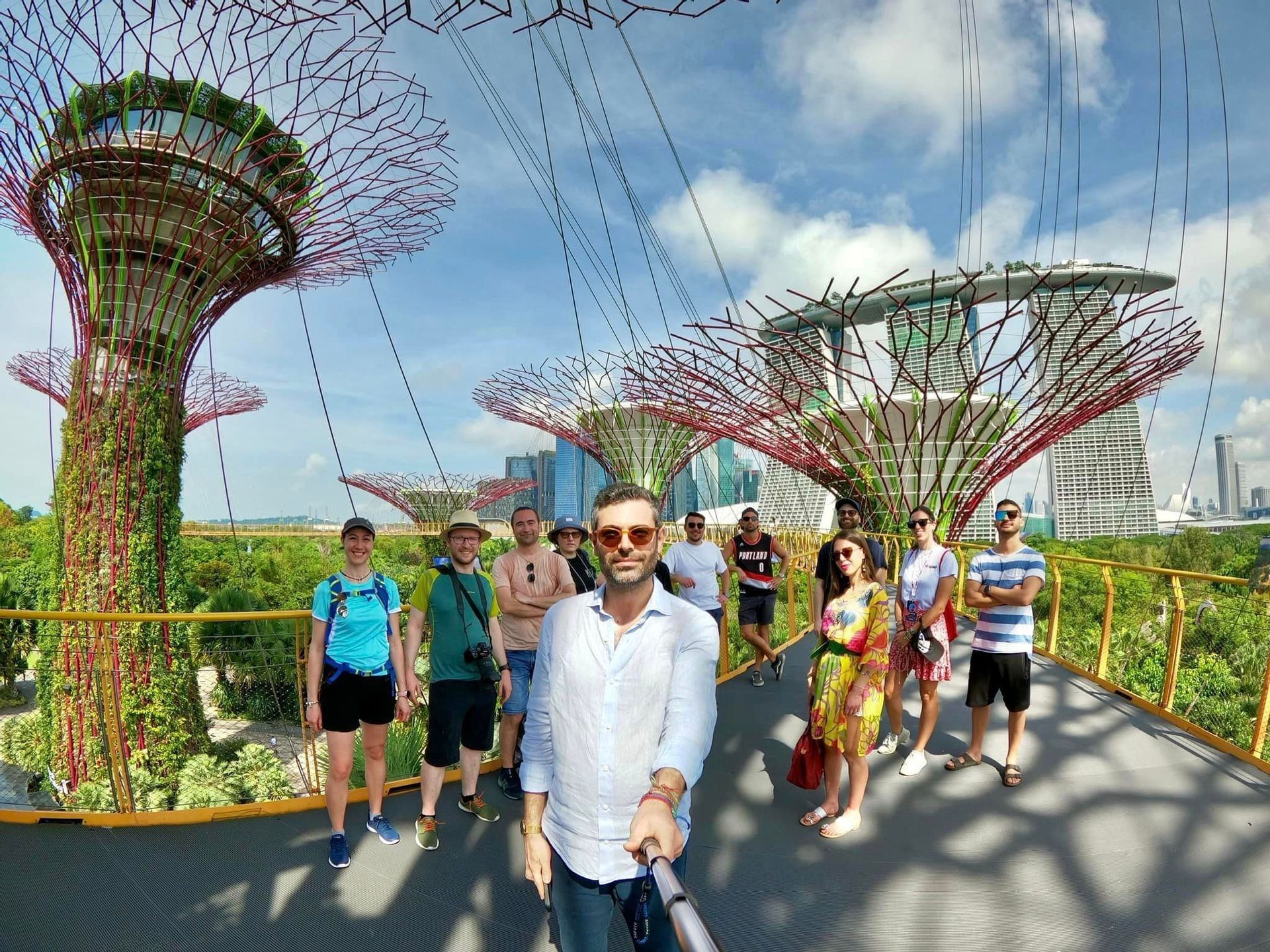 Un viaje en grupo de WeRoad se toma una selfie en una pasarela elevada entre grandes estructuras arbóreas futuristas con un paisaje urbano de fondo.