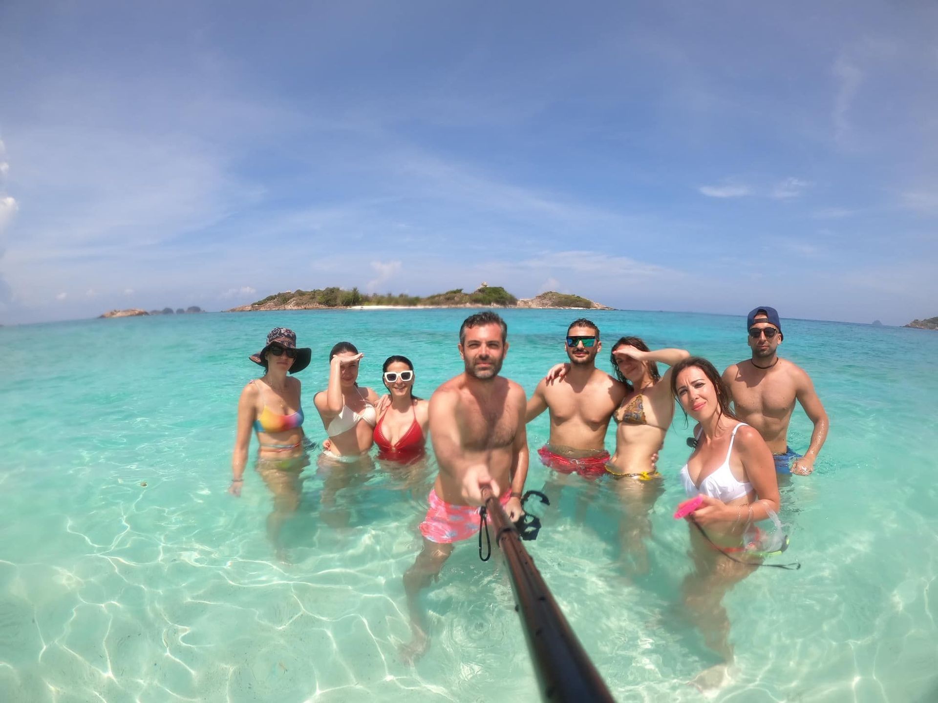 Un grupo de WeRoad se toma una selfie con un palo selfie en aguas claras, poco profundas y turquesas, con islas de fondo.