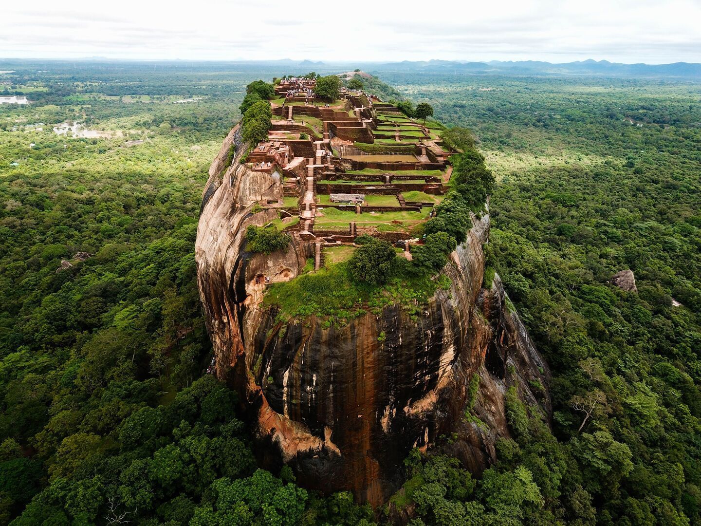 Vista aerea di rovine antiche e giardini costruiti sulla cima di un grande monolite roccioso circondato da una fitta foresta verde