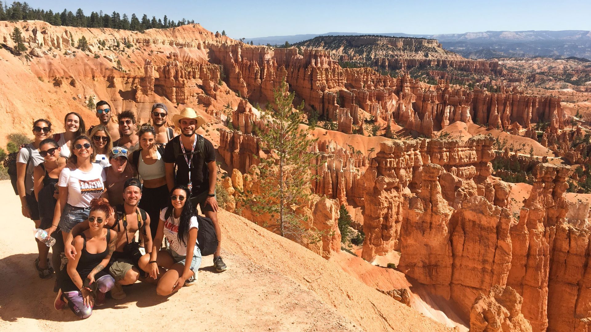 Un gruppo WeRoad in viaggio posa per una foto da un punto panoramico che si affaccia su un vasto canyon con guglie di roccia arancioni.