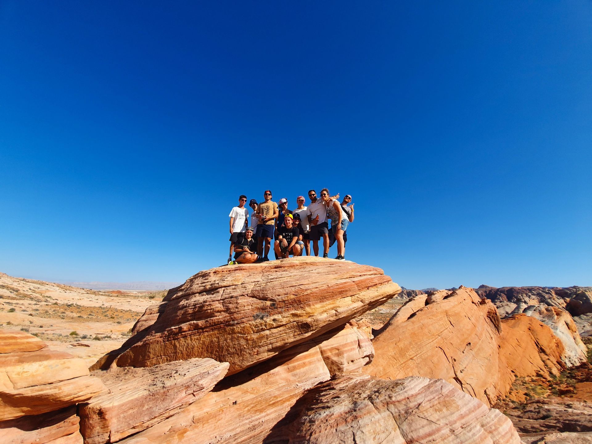 Un gruppo WeRoad in posa su una grande formazione rocciosa rossa in un paesaggio desertico sotto un cielo azzurro.
