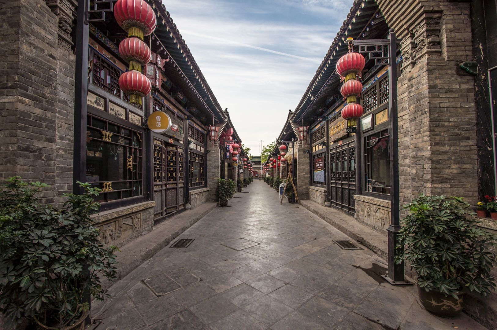 Una calle estrecha y adoquinada flanqueada por edificios tradicionales de ladrillo decorados con farolillos de papel rojos bajo un cielo nublado.