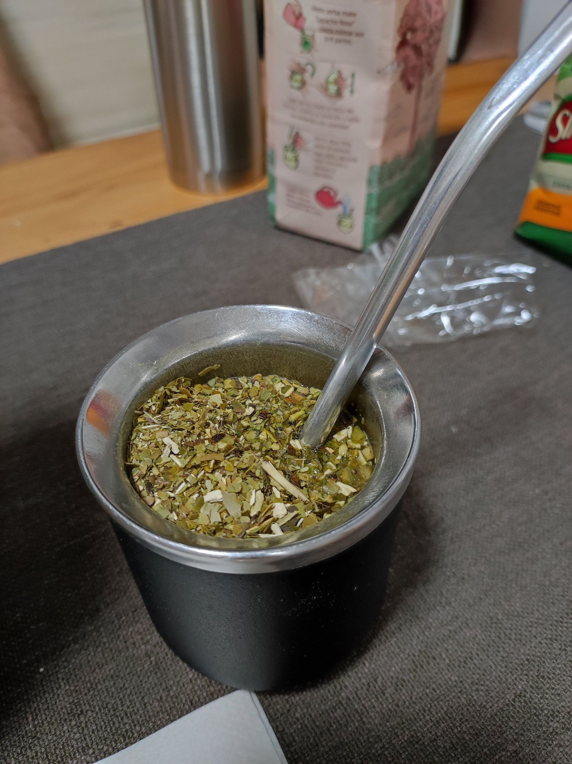 Un primo piano di una zucca da mate nera e argentata riempita con foglie di yerba mate e una cannuccia bombilla di metallo su un tavolo.