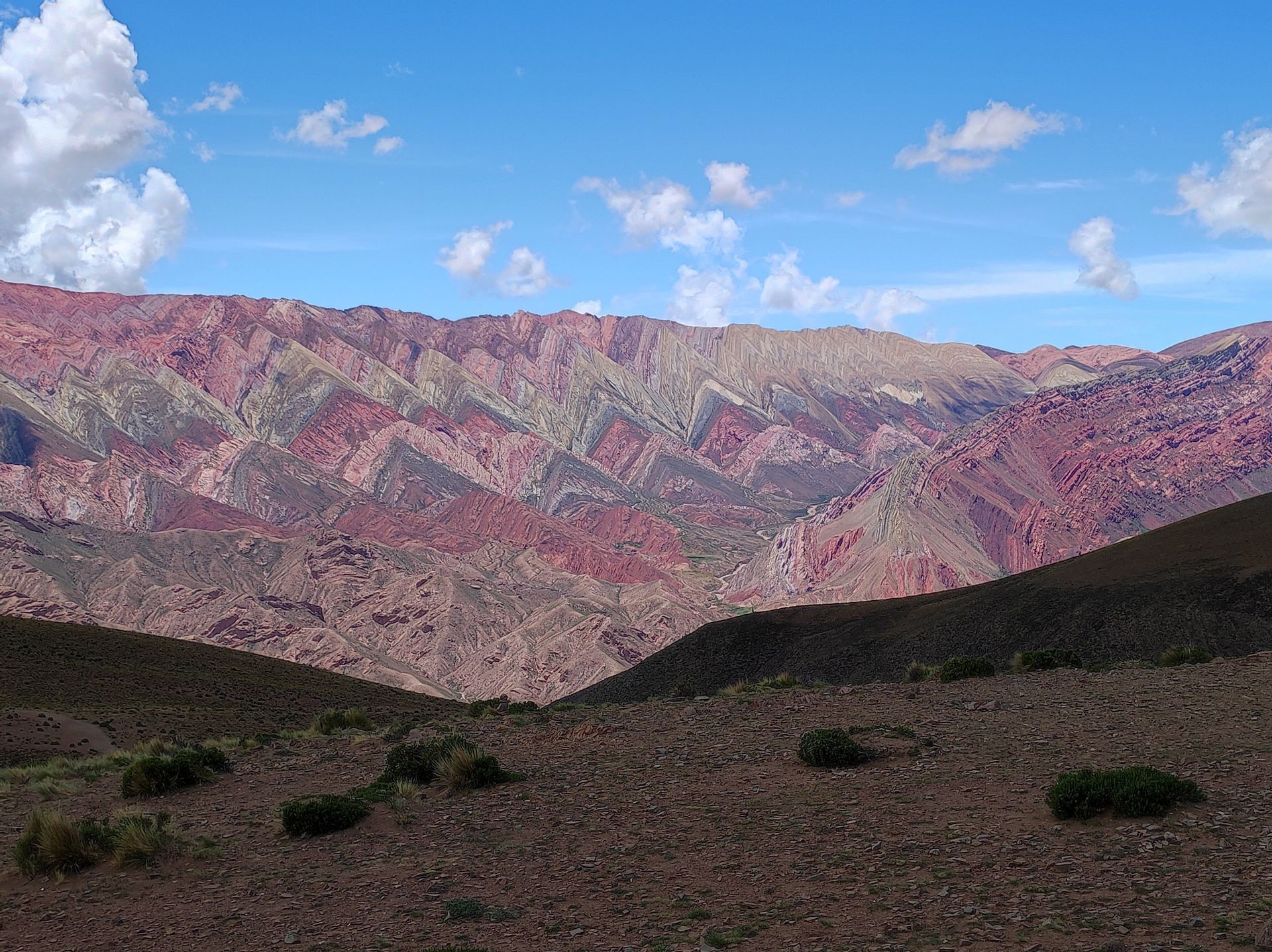 Una catena montuosa con strati a strisce colorate di rosso, viola e beige sotto un cielo blu parzialmente nuvoloso.