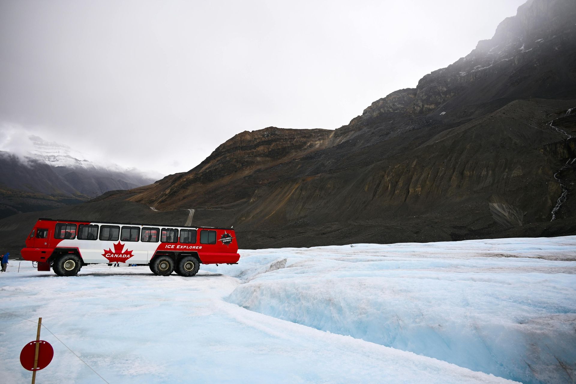 Un voyage de groupe WeRoad à bord d'un bus Ice Explorer rouge et blanc garé sur un vaste glacier au pied de montagnes rocheuses.