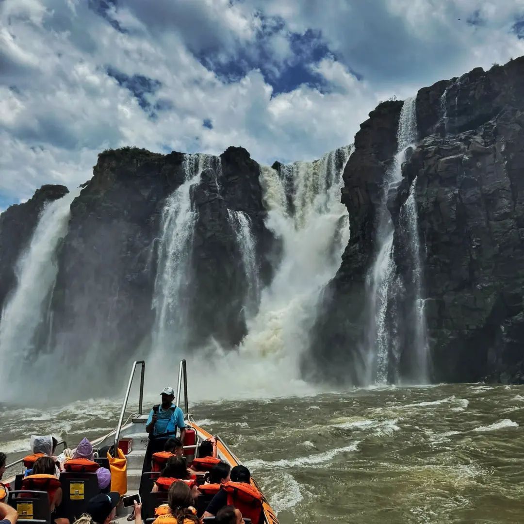 Un viaggio di gruppo WeRoad in barca si dirige su acque agitate verso un'imponente cascata che si getta da una scogliera rocciosa.