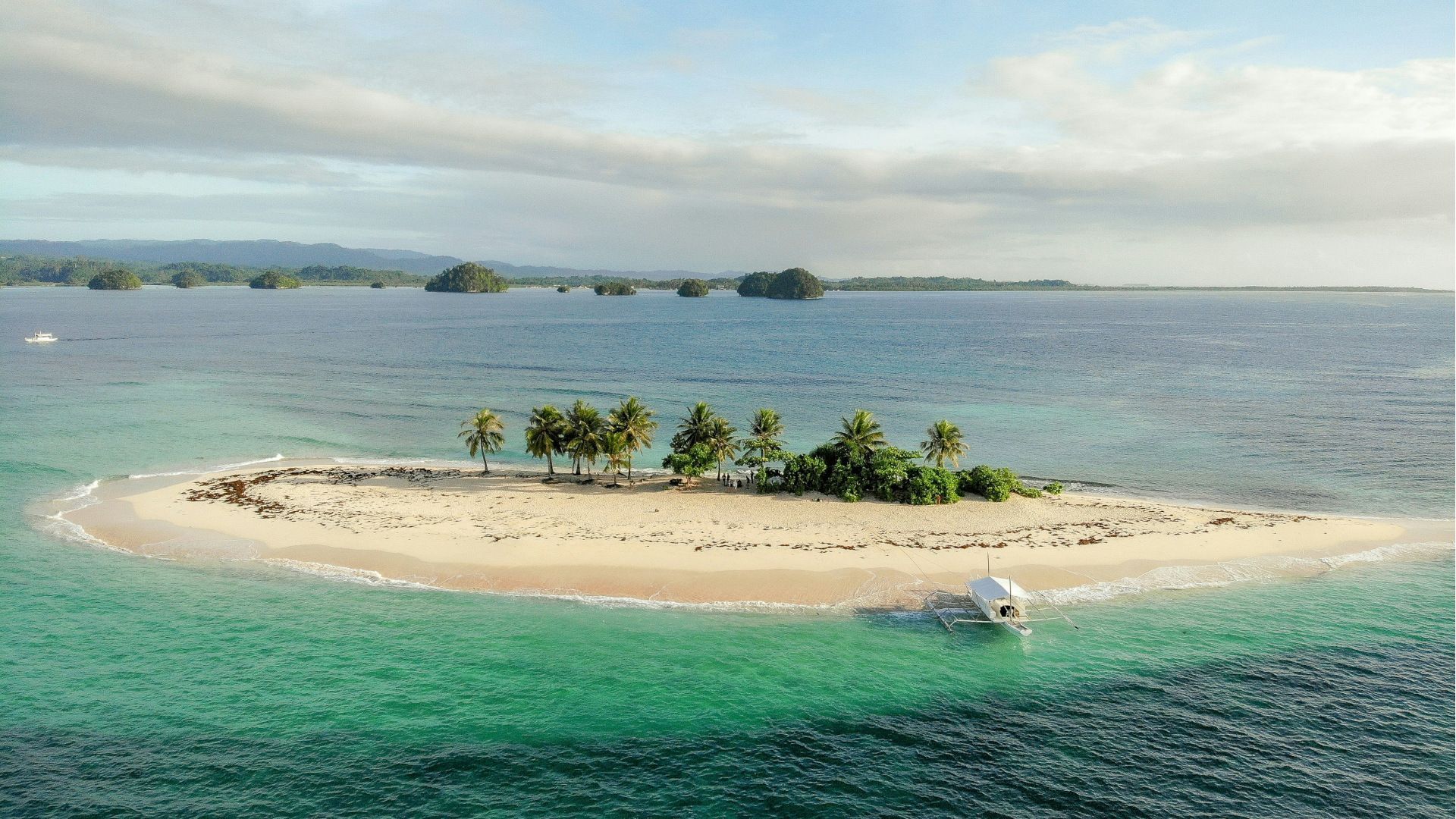 Una veduta aerea di un viaggio di gruppo WeRoad su una piccola isola tropicale, con sabbia bianca, palme e una barca ormeggiata in acqua turchese.