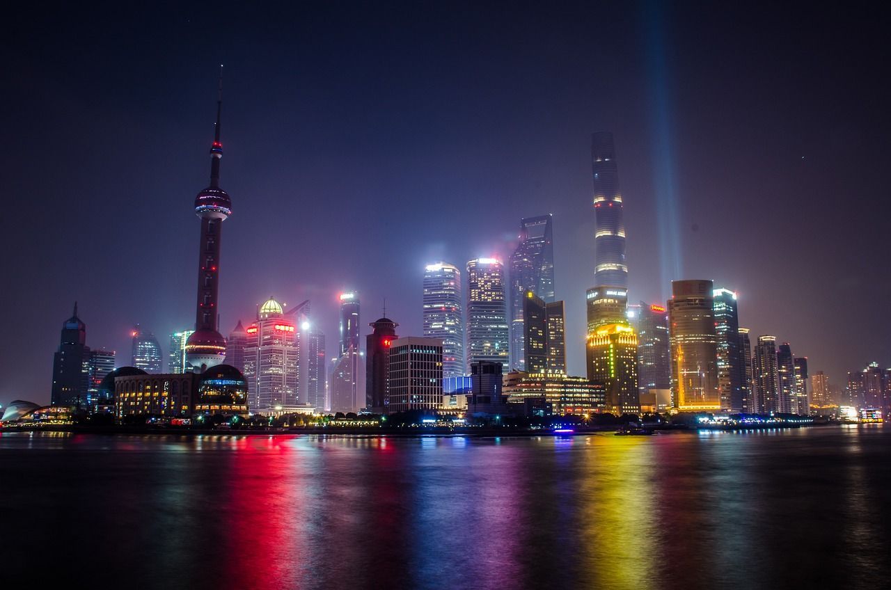 Un ampio skyline cittadino di notte, con edifici illuminati e una torre che riflette luci colorate sull'acqua.