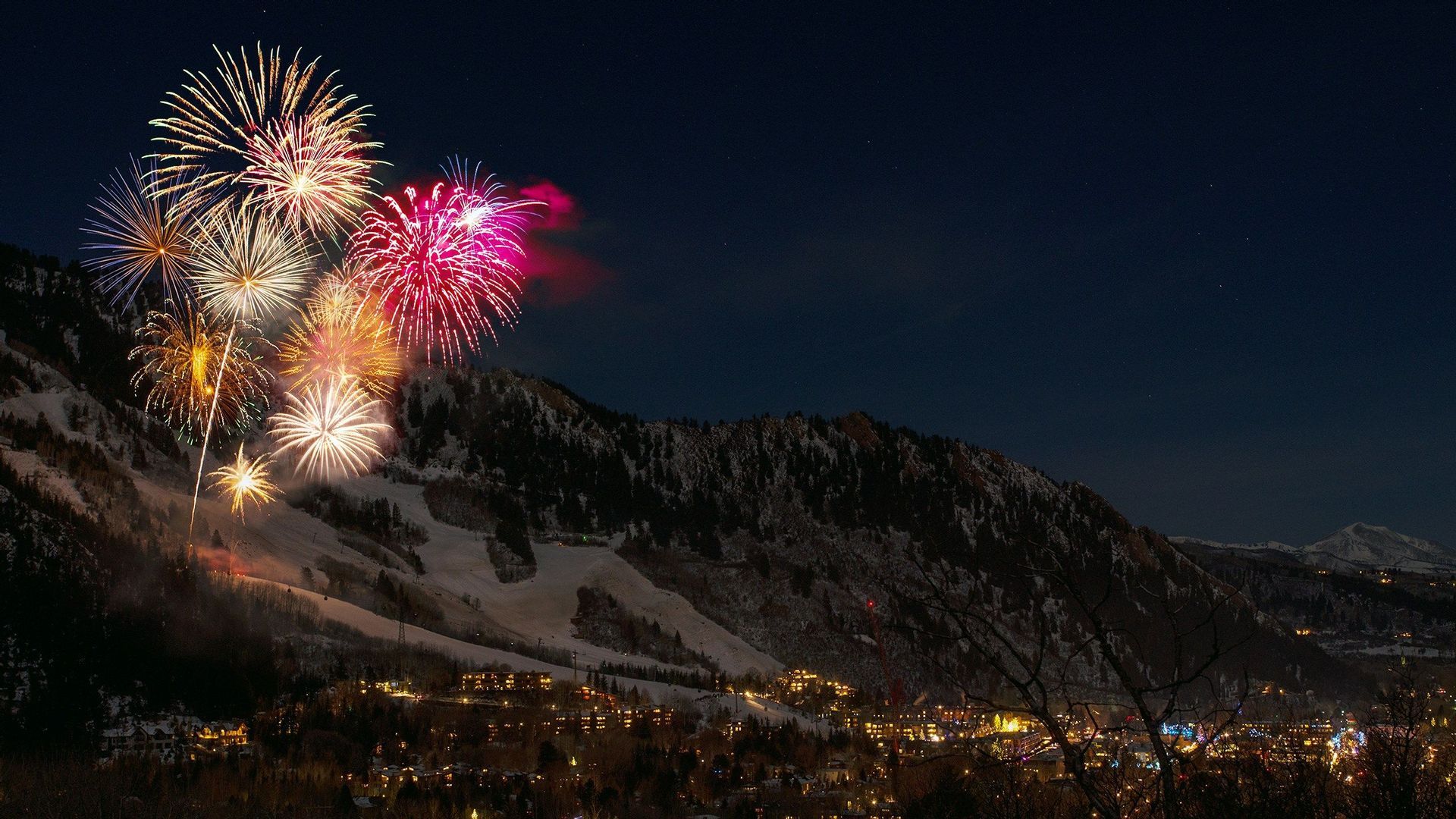Fuochi d'artificio colorati esplodono su un villaggio montano innevato di notte.