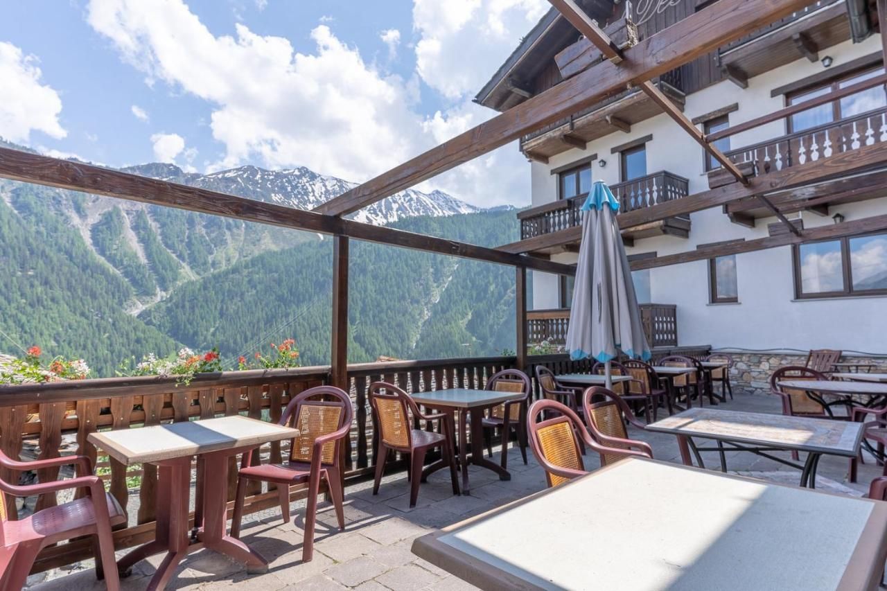 Una terrazza vuota di un ristorante all'aperto con tavoli e sedie, affacciata su una vista di montagne verdi e innevate.
