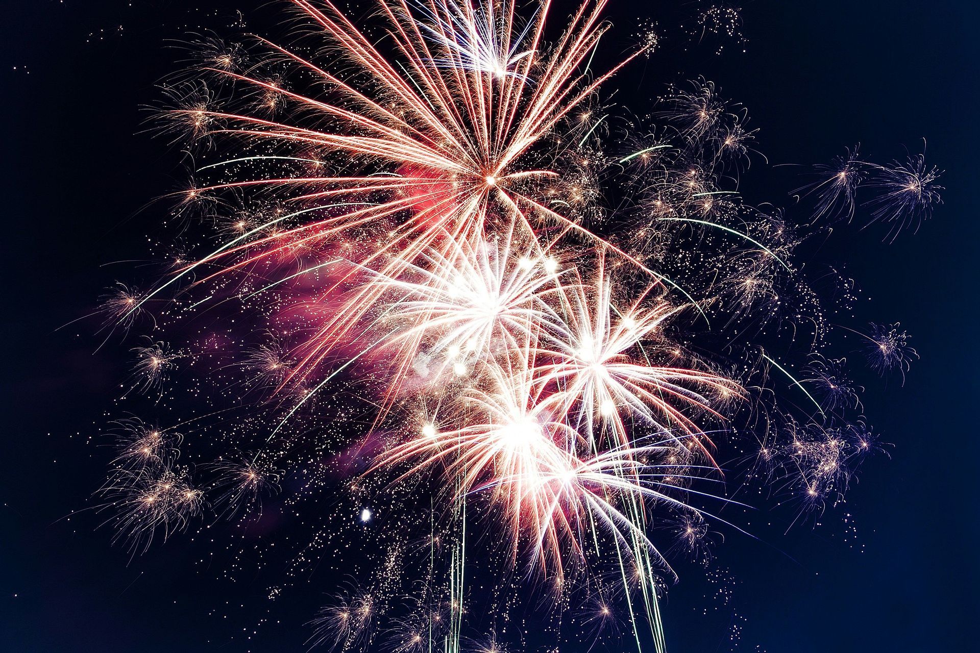 Esplosioni di fuochi d'artificio rossi e bianchi illuminano il cielo notturno scuro con scie e scintille luminose.